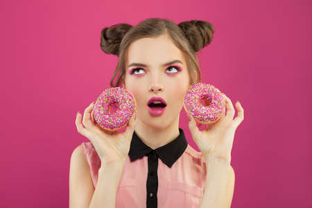Pretty fashion woman holding donut on vivid pink backgroundの写真素材