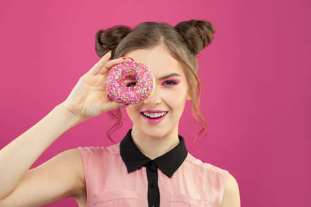 Happy woman holding donut on pink backgroundの写真素材