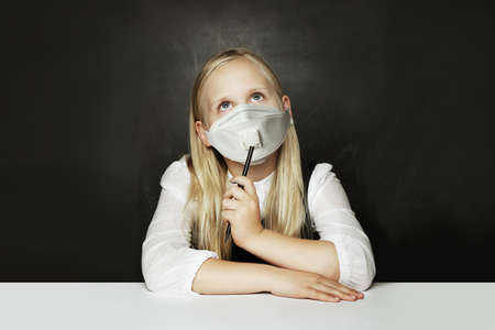 Cute child girl in protective face mask on chalkboard backgroundの写真素材