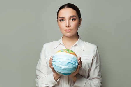 Young woman with a globe earth in medical protective mask. Global pandemic covid-19 conceptの写真素材