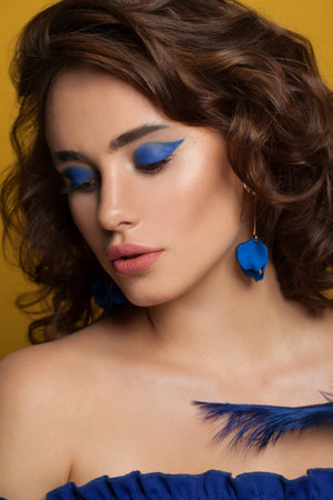 Elegant woman with brown curly hairstyle and makeup on yellow backgroundの写真素材