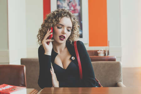 Young beautiful woman using smartphone while sitting at cafeteria. Happy university student female using mobile phoneの写真素材