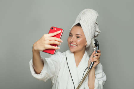 Happy attractive woman taking a shower and making selfie on gray background