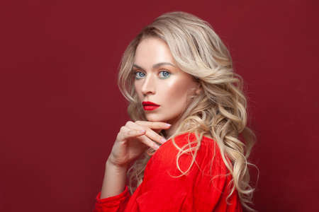 Stylish mature blonde model woman with red lips makeup and healthy curly hair on red banner background, portraitの写真素材