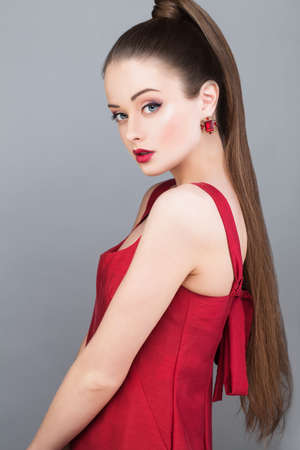 Beautiful glamorous woman fashion model with pony tail hairstyle wearing red dress and golden earringの写真素材