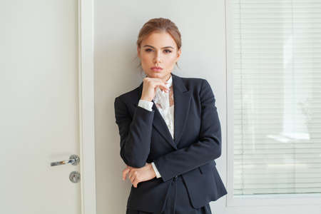Beautiful female blonde business woman CEO in a black suit at the workplace, standing confidently...