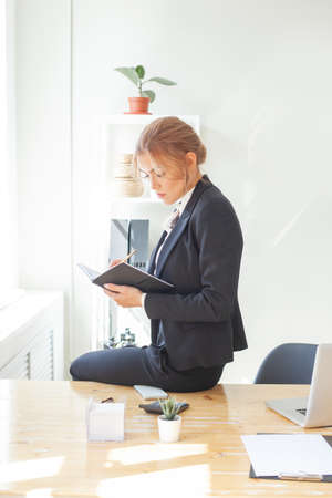 Business Woman in black suit with a notebook and a pen in her hands planning, analyzing and writing notesの写真素材