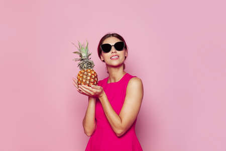 Happy young woman with pineapple looking up over pink studio background