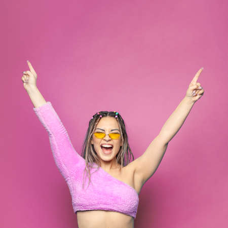 Happy young woman having fun with hands up on colorful pink background