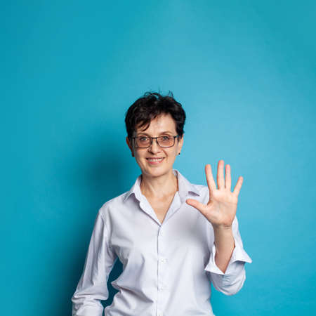 Happy mature woman with short hair counting and showing five with fingers on blue background