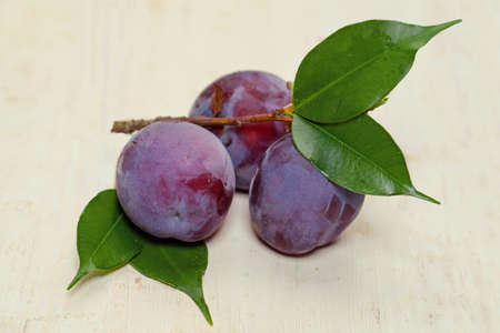 Sweet Purple Plum with green leaves on wooden tableの写真素材