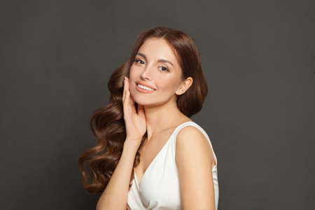 Portrait of beautiful attractive fashion model with long shiny wavy brown hair smiling on black backgroundの写真素材