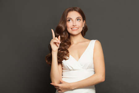 Stylish pretty woman fashion model pointing up on gray studio background