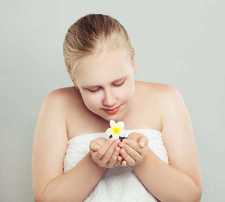 Pretty teen girl holding natural tropical flower and spa stone. Spa, wellness, massage, facial treatment and skin care conceptの写真素材