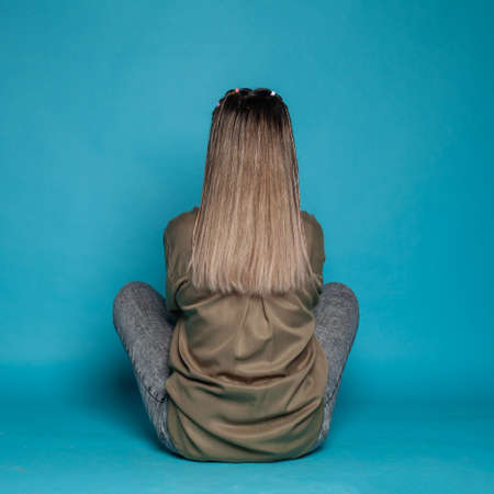 Female back on blue studio background. Young woman sitting on floor
