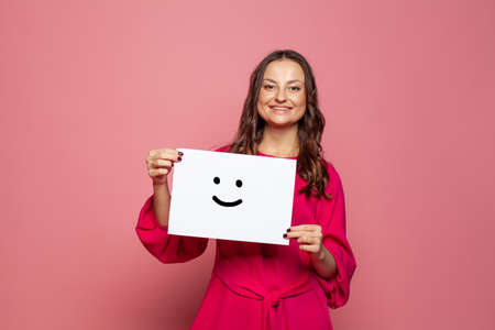 Young woman holding white paper with smile sign on pink background