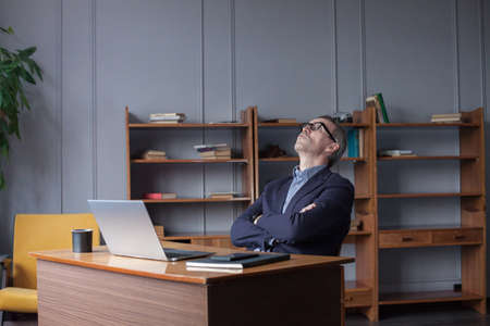 Middle aged man relaxing sitting in officeの写真素材