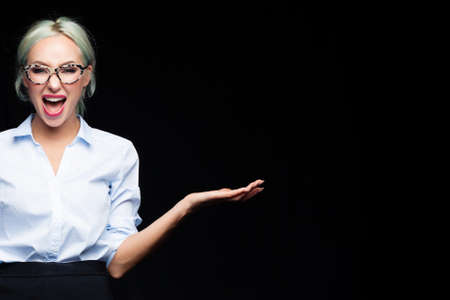 Blonde business woman screaming and showing empty open hand with blank copy space on black studio backgroundの写真素材