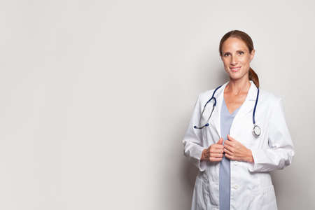 Pretty woman doctor hospital worker looking at camera and smiling against grey studio wall banner...