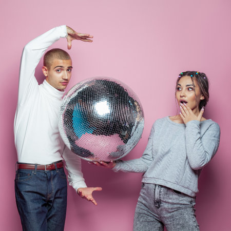 Young happy woman and man with disco ball posing on pink backgroundの写真素材