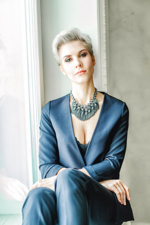 Portrait of businesswoman in blue suit sitting on windowsill