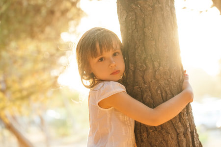 Portrait of child girl hugging the tree on the background of parkの写真素材