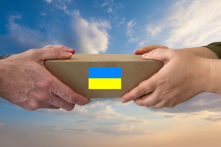 A volunteer hands holding a box of aid for Ukrainian refugees and citizens who find themselves in a war between Ukraine and Russia. Humanitarian aid and support for Ukraine conceptの写真素材