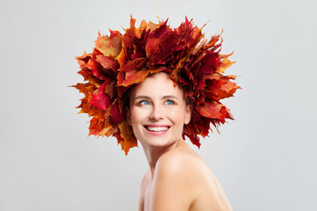 Autumn woman portrait. Beautiful young model with fall leaves, healthy shiny fresh clear skin and makeup smiling on white backgroundの写真素材
