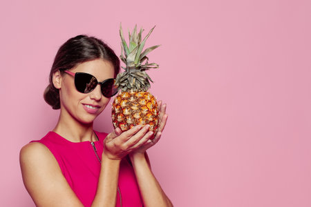 Pretty brunette woman in sunglasses with pineapple fruit on pink backgroundの写真素材