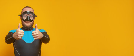 Closeup portrait of diver diving guy showing thumb up against colorful orange studio wall backgroundの写真素材