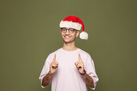 Happy Christmas man Santa wearing blank t-shirt pointing up on green studio wall backgroundの写真素材