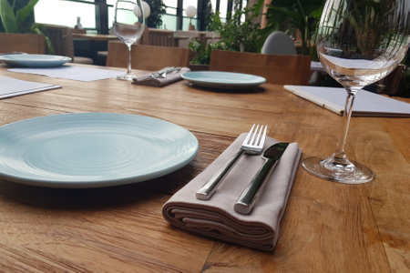 Empty flat plate, empty glass and cutlery on brown wooden table. Table setting in restaurant.