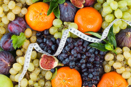Diet concept with measuring tape, orange tangerine, figs and grape fruit mix with green leaves. Healthy food backgroundの写真素材