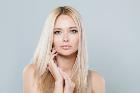 Perfect blonde woman with long straight hair and clean fresh pure perfect skin isolated on gray background, studio portraitの写真素材
