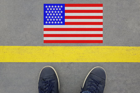 Word Start written on an asphalt road with the American flag and legs in shoes. Immigration and...