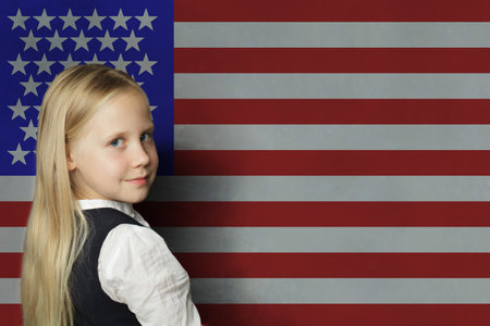 Happy young child girl student in front of USA flag background, US conceptの写真素材