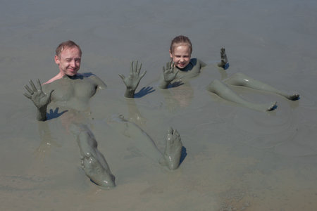 Happy people on mud geyser resort with therapeutic mud outdoor. Dirty family child girl and dad in...