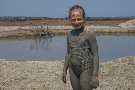 Happy child girl resting on mud geyser resort with therapeutic mud outdoors