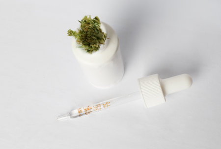 Close up of white dropper bottle for cannabis oil with marijuana plant on white background, top view. Bottle product of CBD and THC hemp oilの写真素材