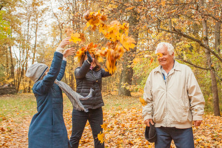 Happy grandfather, muther and little child girl having fun with yellow autumn leaves on nature...