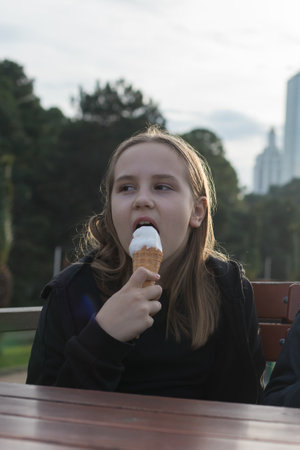Portrait of young girl holding a vanilla ice cream in cone sitting on table in city street cafe outdoorsの写真素材