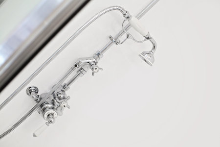 Close-up of bathroom with a white wall and a chrome shower head, interior background