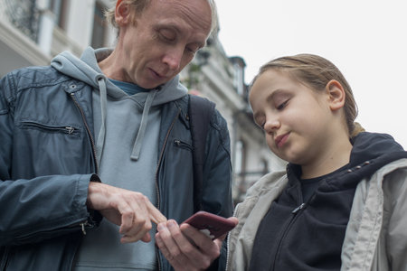 Close-up portrait of father and child using smartphone booking taxi or looking at a map outdoors. Happy family, travel and weekend conceptの写真素材