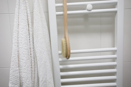 White bathroom interior detail. Heated towel rail with white cotton towel and brush