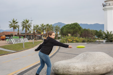 Cheerful child young girl throwing flying disc and having fun outdoors. Happy childhood, sport and leisure activity conceptの写真素材
