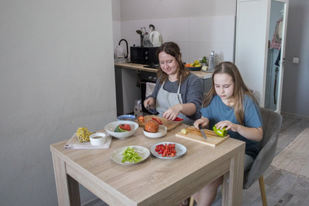Beautiful daughter and her mother cooking in domestic kitchen together, family lifestyle portraitの写真素材