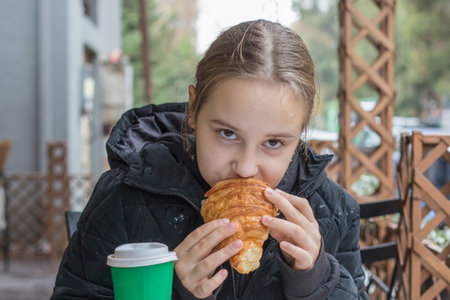 Young child girl eating croissant and drinking coffee in street cafeの写真素材