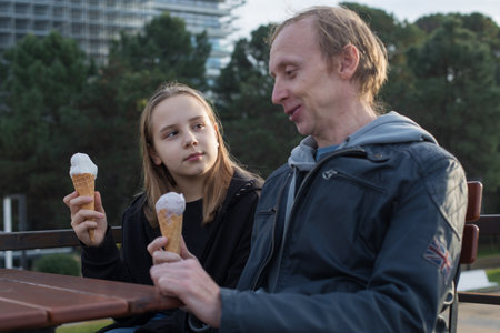 Happy father and daughter eating ice cream sitting in city street cafe outdoors. Happy family, childhood, leisure activity and weekend concept.の写真素材