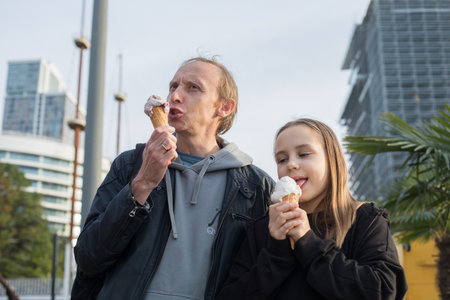 Little child daughter and her father walking and eating ice cream outdoors. Happy family, childhood and weekend conceptの写真素材