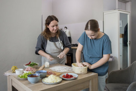 Portrait of child girl daughter and mother preparing dough for pizza and smiling while baking in kitchen at home, family togetherの写真素材